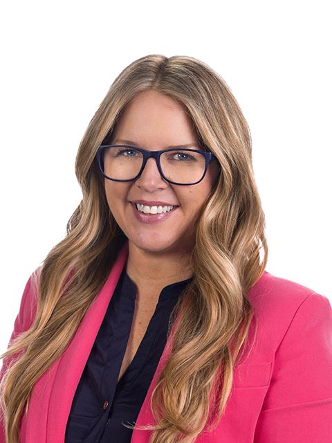 Portrait of Commissioner Clasen with long, wavy hair, wearing glasses, pink blazer over a navy top.