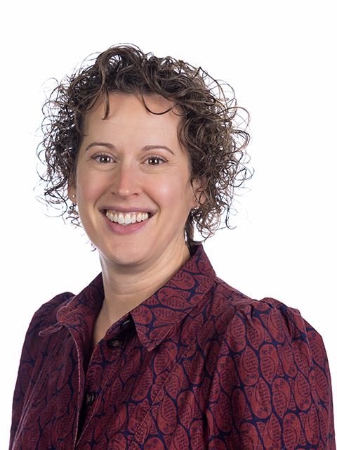 Portrait of Commissioner Cox with curly hair, wearing a red patterned shirt, on white background.